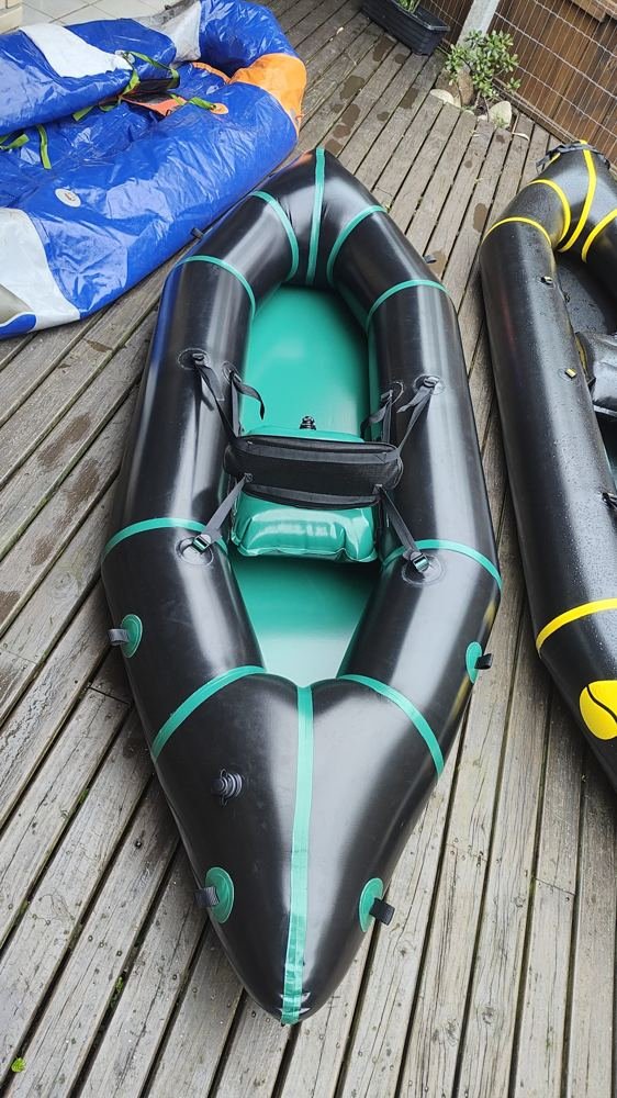 Packraft preto com faixas e fundo verdes visto de cima, com assento inflável e encosto